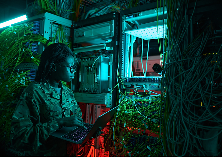 soldier stands with laptop surrounded by wires and control panels