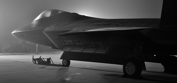 n Air Force F-22 Raptor stealth jet sits on a flight line at night