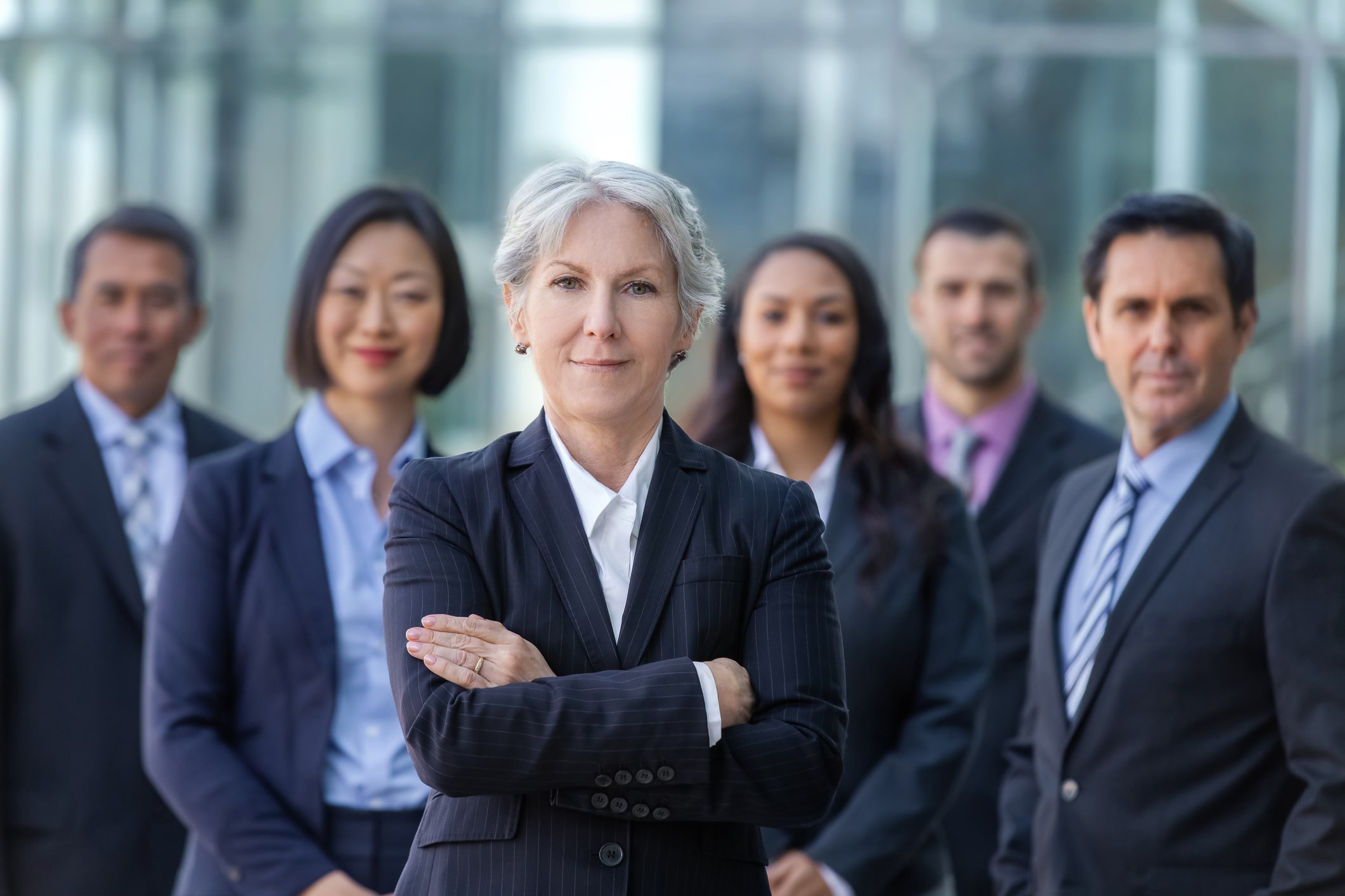 business woman leader stands in front of other coworkers with her arms crossed